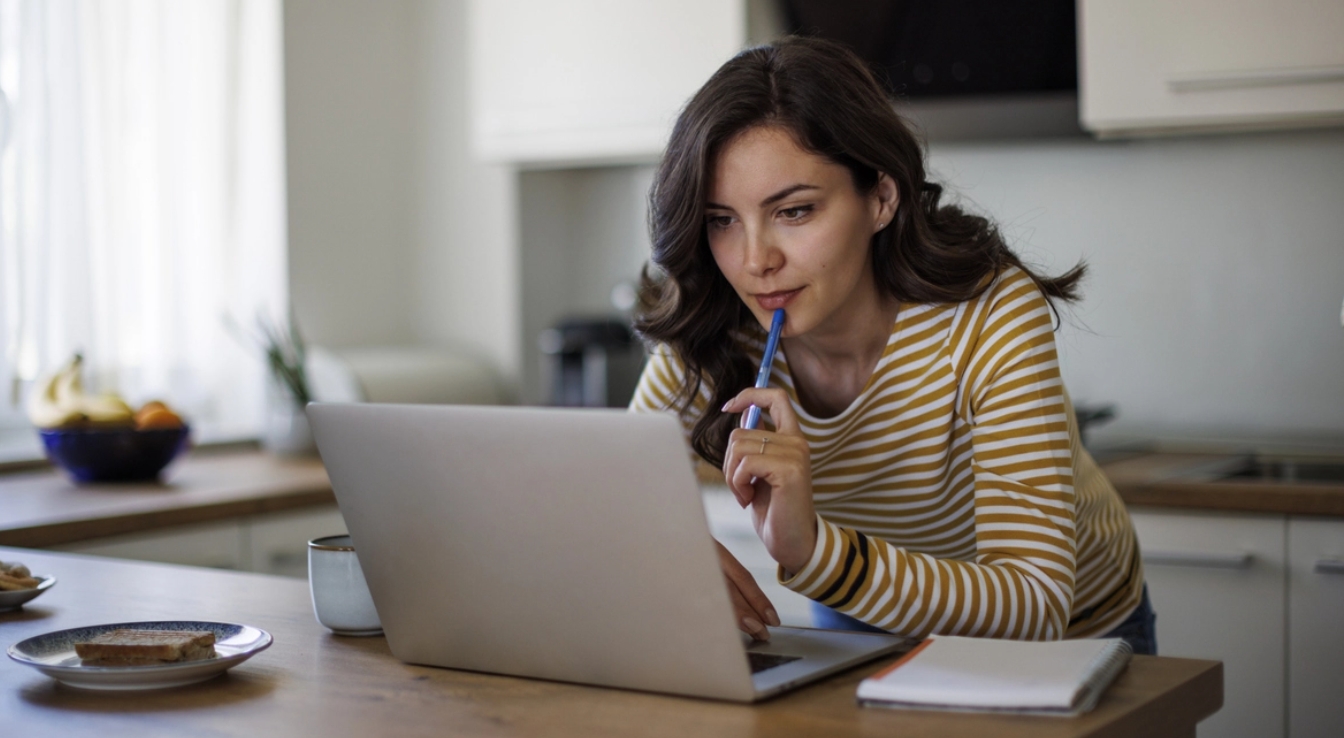 Woman views laptop with pen in her hand
